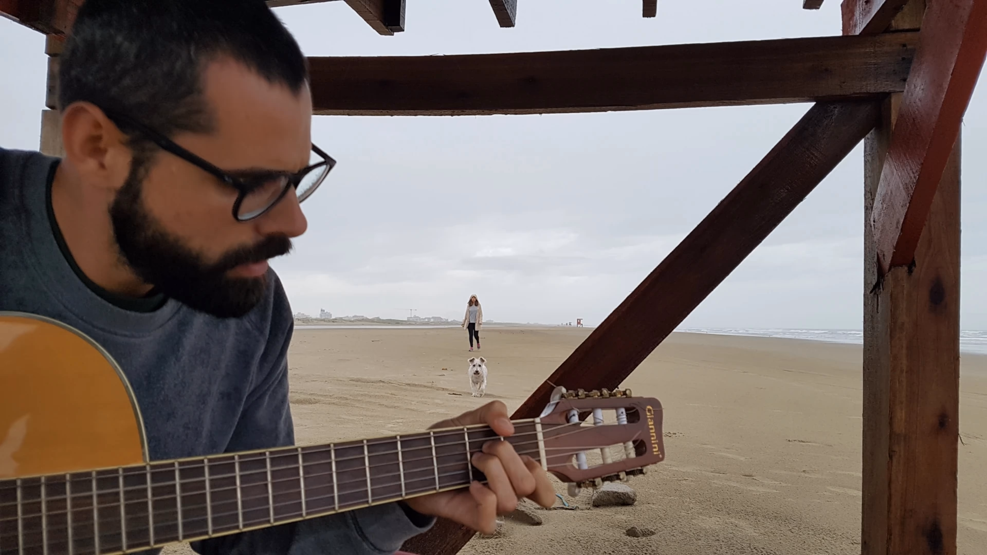 Foto tirada na beira da praia, em primeiro plano o meu irmão tocando violão, em segundo plano meu cachorro e minha namorada
